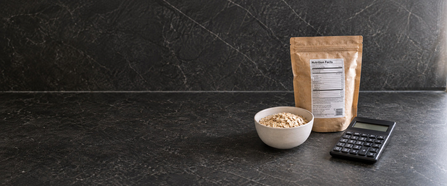 A bag of oats with a nutrition label, a bowl of oats and a calculator on a dark countertop.