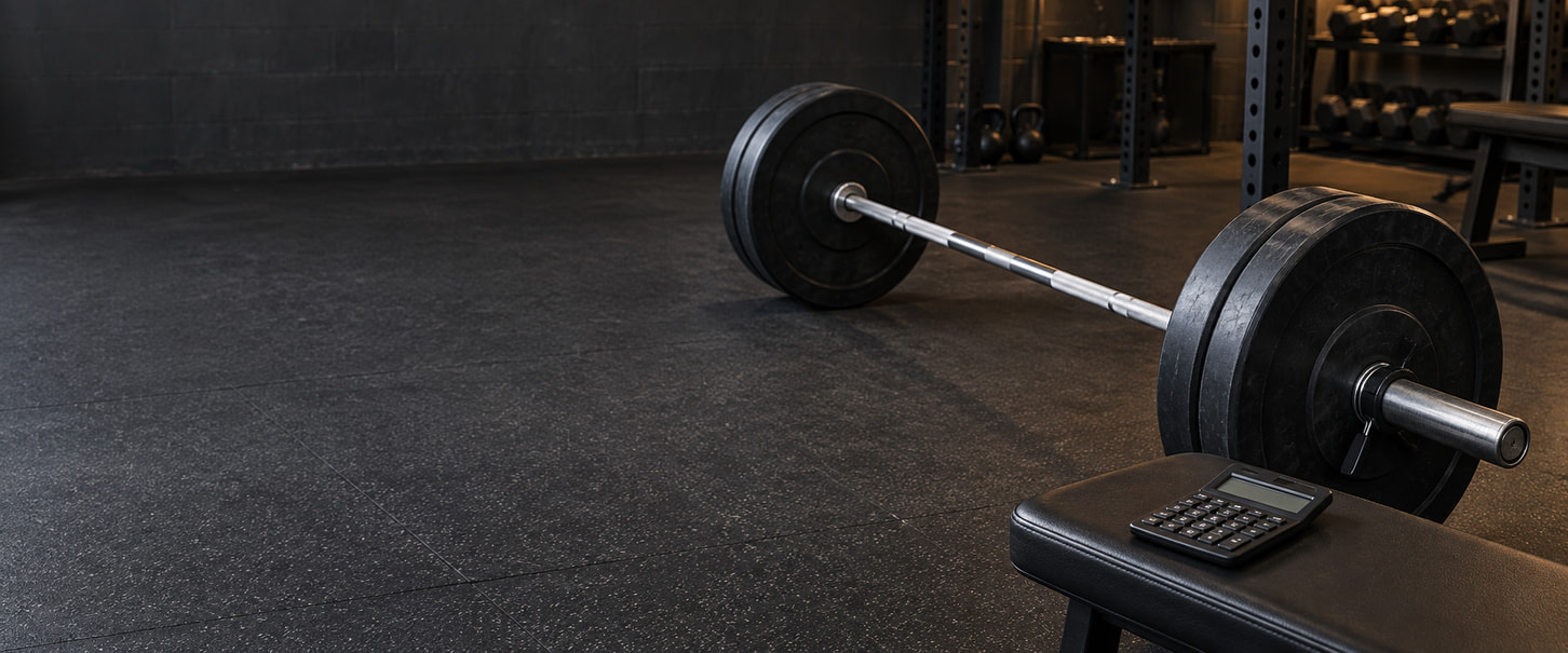 A loaded barbell on a gym floor beside a calculator resting on a padded bench.