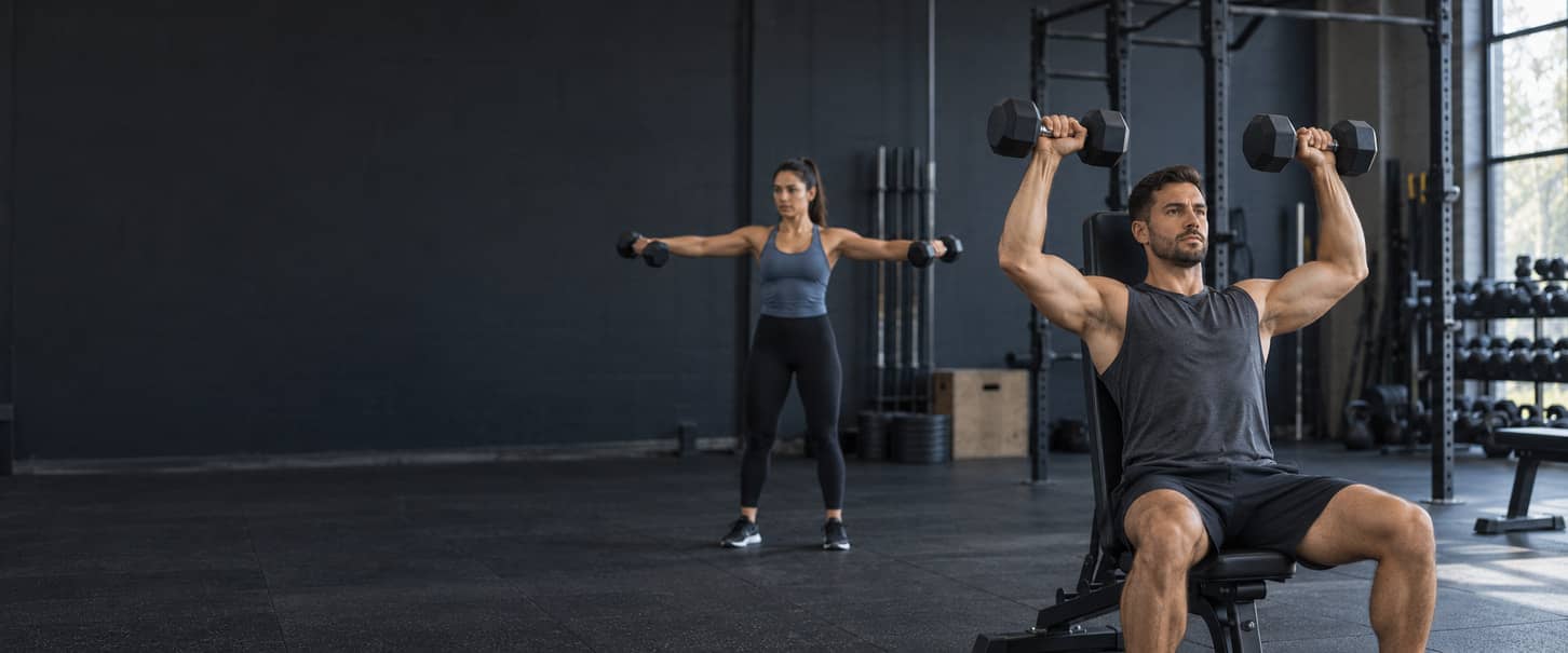 Man performing a seated dumbbell shoulder press with a woman doing lateral raises behind him