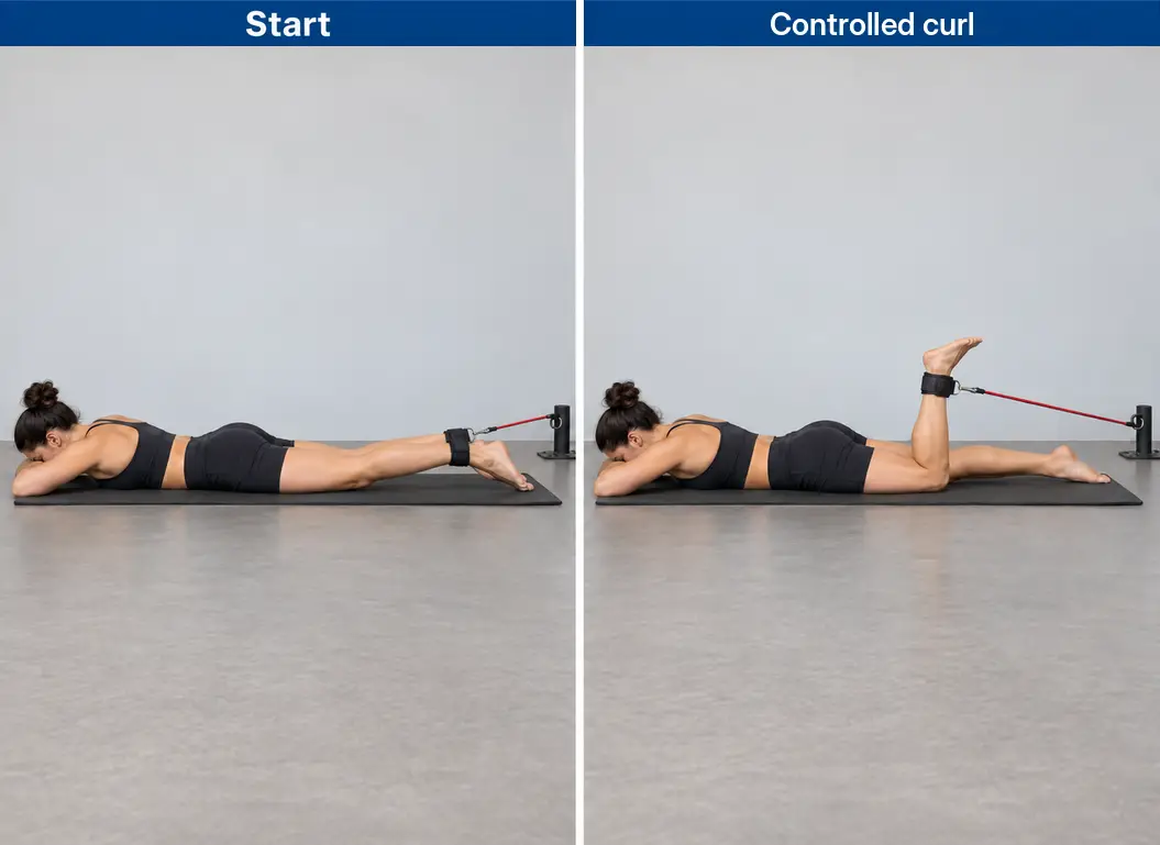 Prone single-leg band curl with an ankle attachment connected to a fixed anchor beyond the feet, showing the working knee bending while the thigh stays supported.